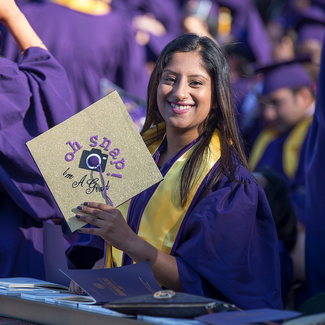 Graduate at Commencement. Her cap says "Oh, snap! I'm a grad." with a camera.