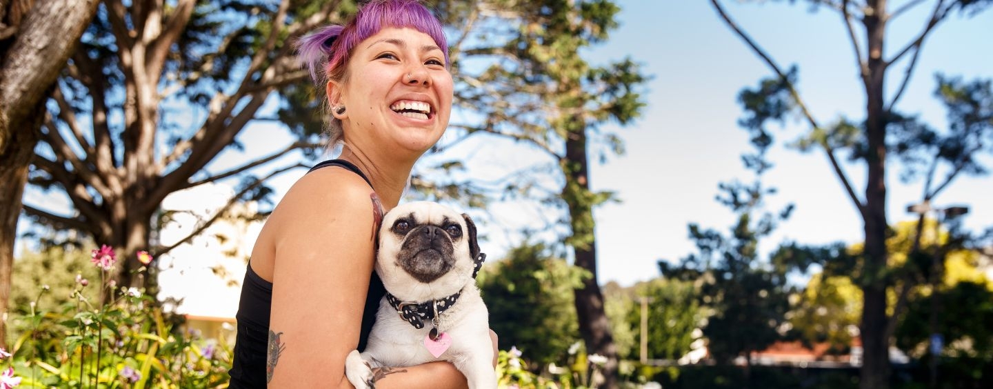 Student with purple hair holding a pug dog on campus