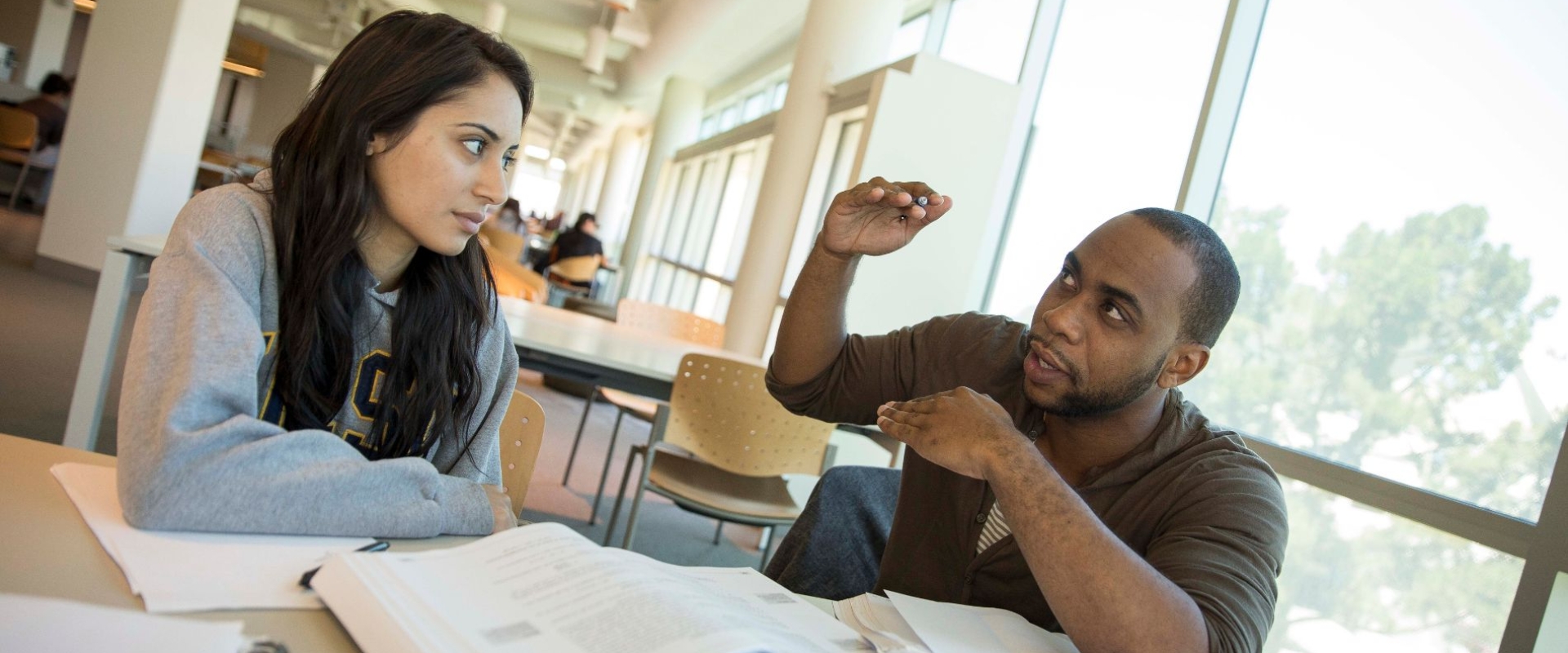 Student gestures with his hands while studying with a partner in the library