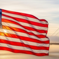 American flag backlit by evening sun and the Golden Gate Bridge in the distance